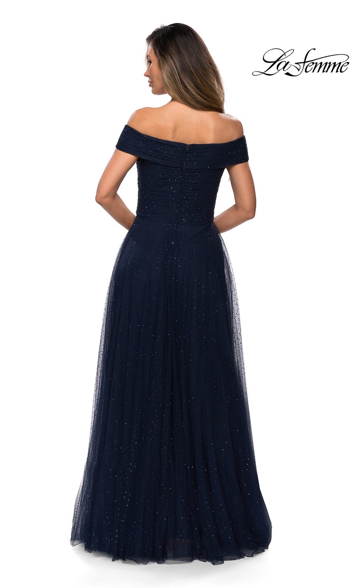 A woman faces away in a navy blue off-the-shoulder tulle gown with subtle sparkles. The fitted bodice and skirt define Long Formal Dress: La Femme 28051. La Femme logo shown.